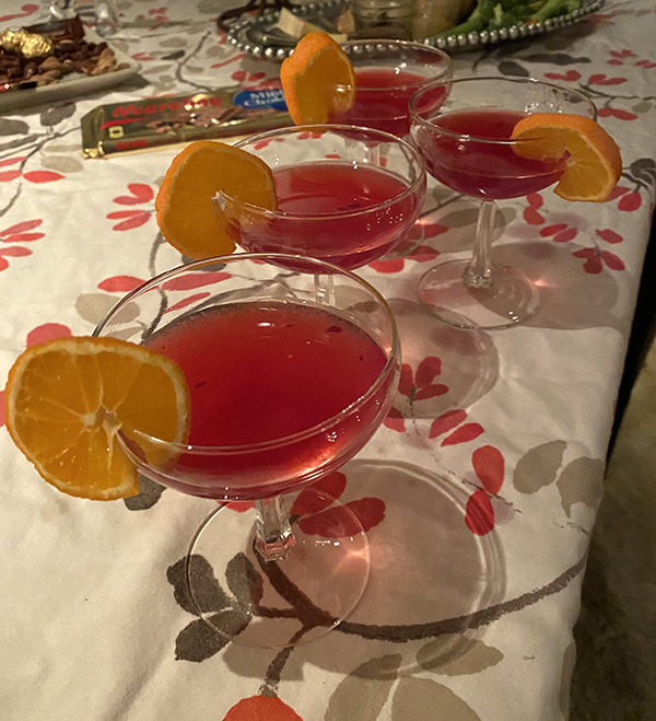 Bright red festive cocktails garnished with orange slices sit on a holiday table.