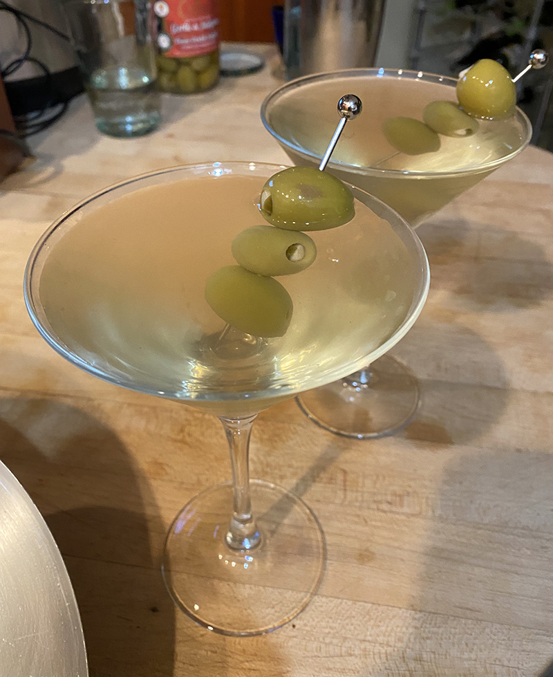 Two dirty martinis sit on a wooden countertop.
