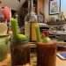 Two Bloody Nöel drinks accompany a burger and a bottle of mezcal on a kitchen counter.